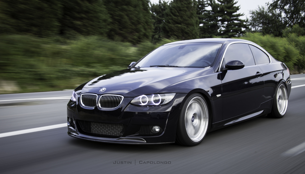 Ein schwarzer BMW fährt auf einer Straße mit Bäumen im Hintergrund.