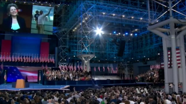 Eine große Zuschauermenge sitzt einer Bühne mit einem Rednerpult, Mikrofon, Flaggen, einem Overhead-Bildschirm und einer Lichtanlage gegenüber, während es scheint, als fände ein Präsidenten-Debatte statt.