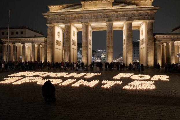 Eine Gruppe von Menschen steht vor dem beleuchteten Reichstagsgebäude in Berlin, Deutschland, umgeben von Gebäuden, Pfählen und Lichtern, und die Wörter 'Kampf für die Freiheit' sind auf dem Boden vorne geschrieben.