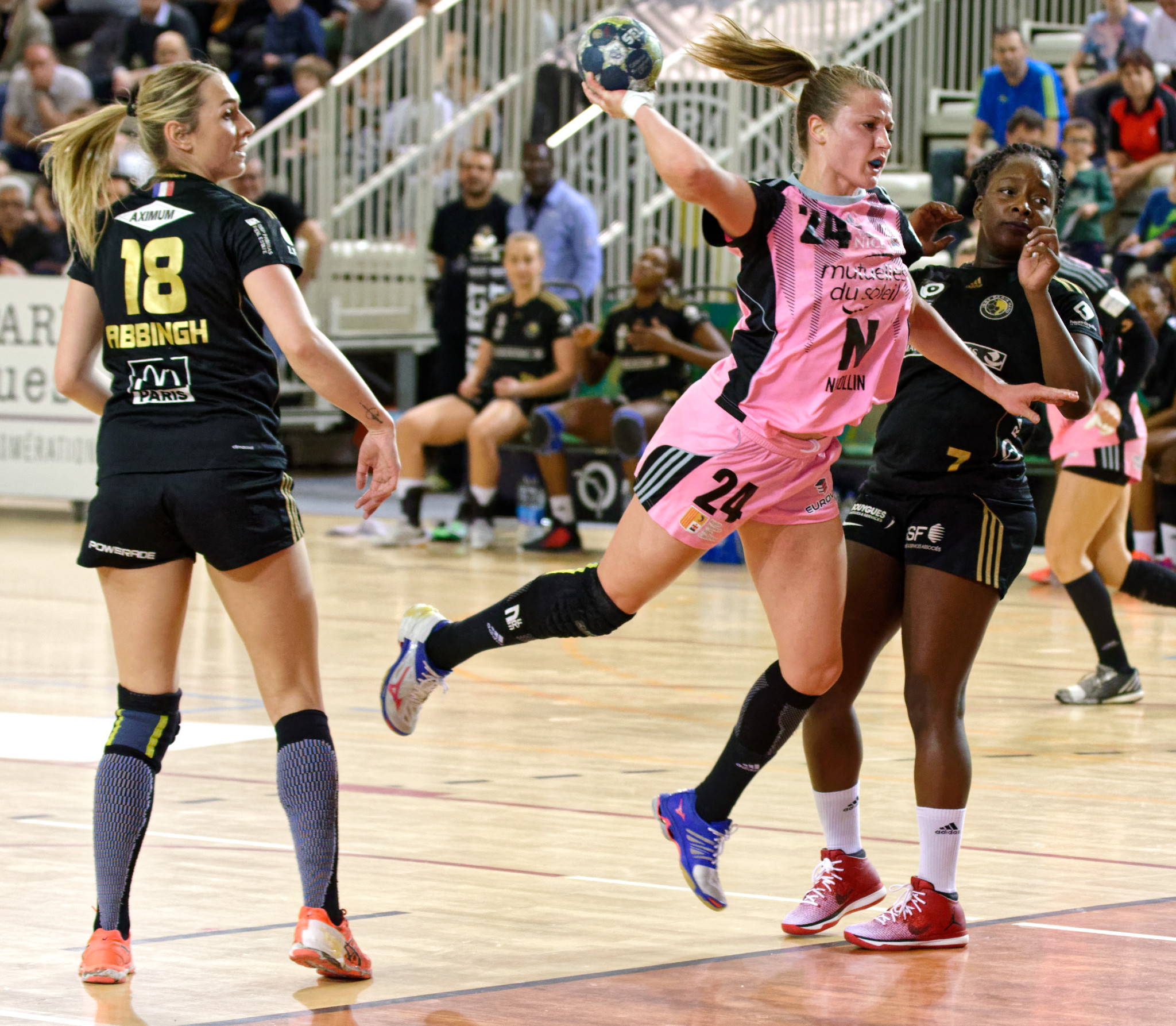 Eine Gruppe von Frauen beim Handballspielen auf einem Platz, mit Zuschauern im Hintergrund.