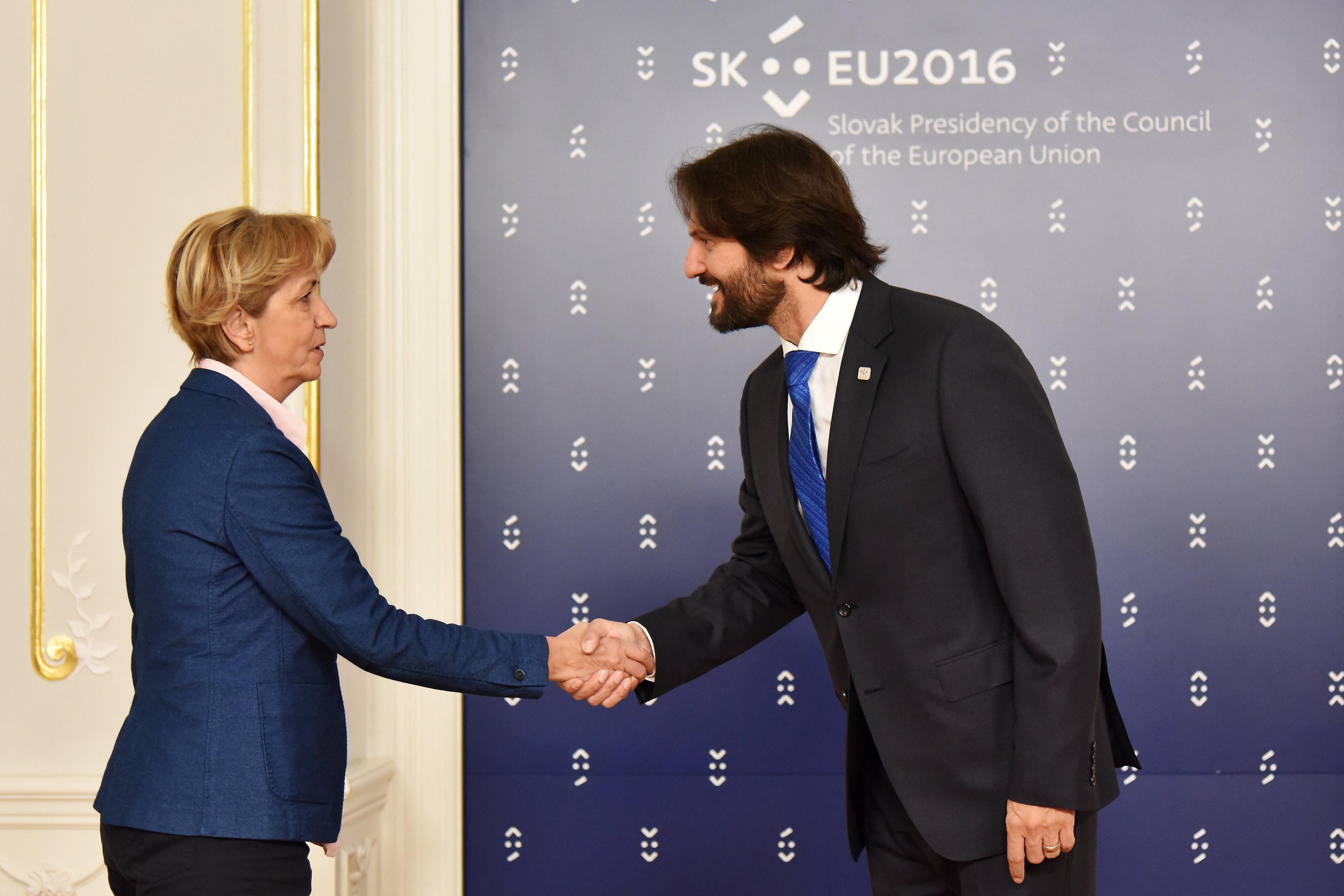Bundeskanzlerin Angela Merkel und Bundespräsident Joachim Gauck schütteln sich die Hände vor einer Wand mit einem "EU-Gipfel"-Schild und einer Tür im Hintergrund, beide lächeln.