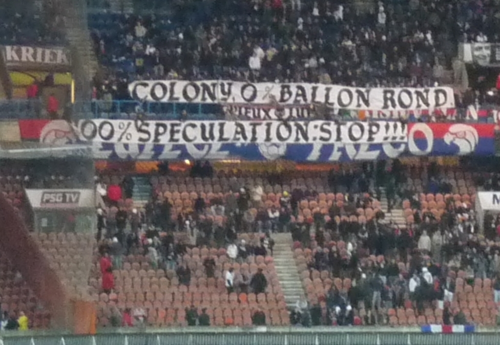 Ein Stadion voller Menschen, Banner und St├╝hle, mit einem Zaun unten und einer Treppe links.