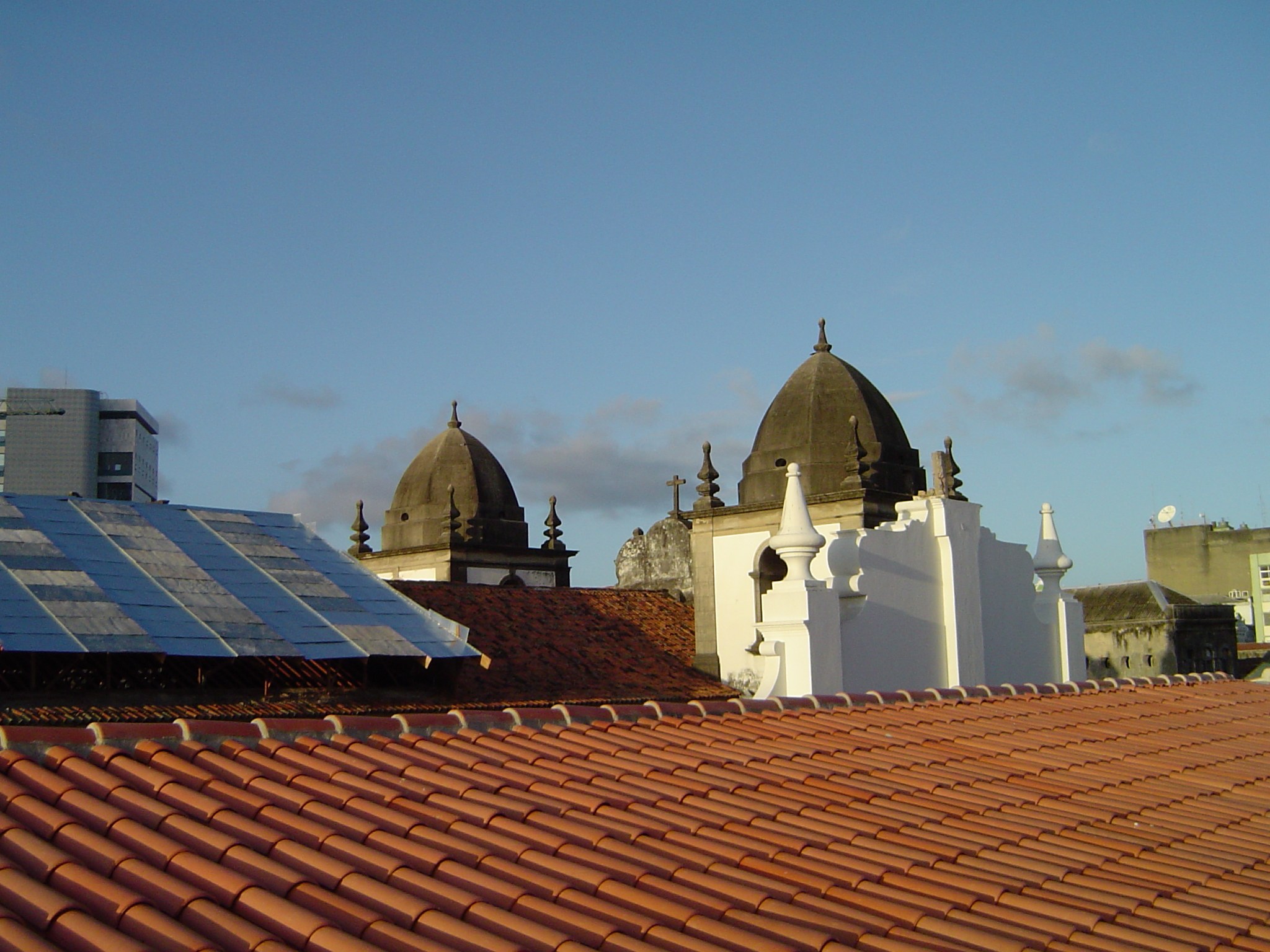Stadtpanorama mit einigen Gebäuden im Vordergrund, Solarpanels auf einem Dach und einem blauen Himmel im Hintergrund.