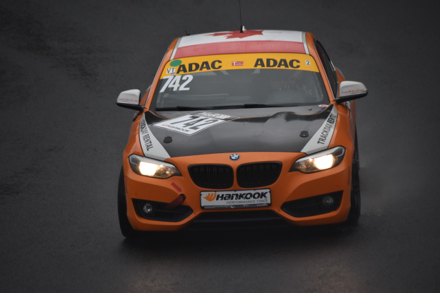 Oranges BMW-Rennfahrzeug mit Text und Zahlen auf einer Rennstrecke.