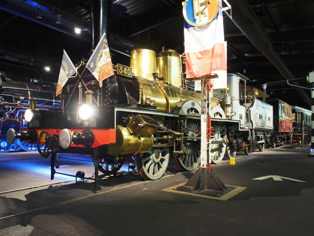Eine alte Dampflokomotive in einem Museum ausgestellt, umgeben von Fahnen, Stangen, Lichtern und anderen Gegenständen, mit einer sichtbaren Decke oben.