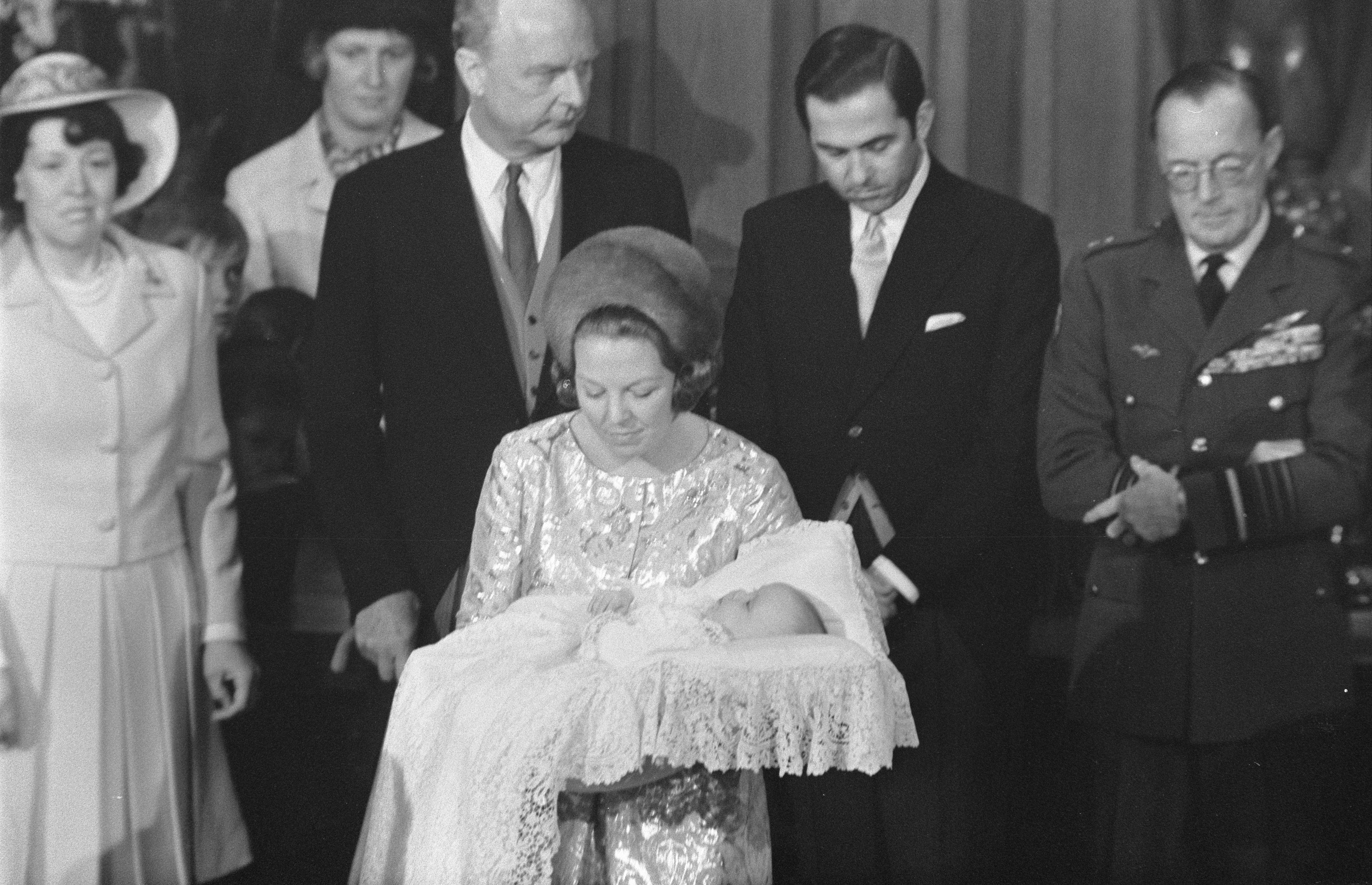 Königin Elizabeth II. hält ihren neugeborenen Prinz Philip in den Armen, während Prinz Philip, Herzog von Edinburgh, neben ihr in einem Anzug und einer Krawatte steht, vor einem Vorhanghintergrund.