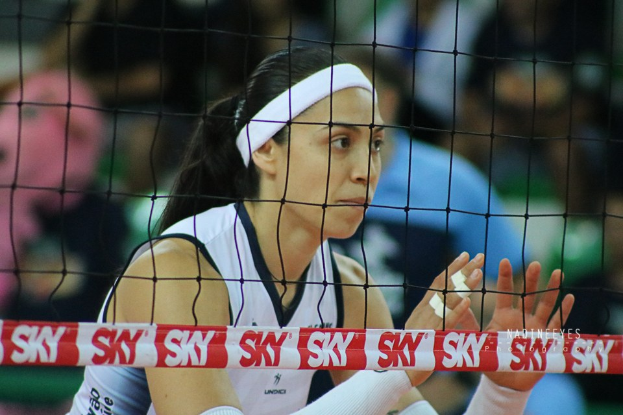 Frau Volleyballspielerin in Aktion auf einem Feld, die eine Uniform trägt, mit einem Netz im Vordergrund und einem unscharfen Hintergrund.
