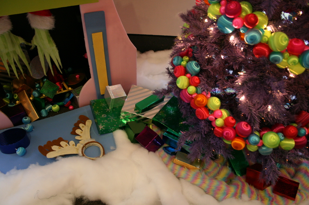 Eine Indoor-Szene mit einem Weihnachtsbaum mit Lichterkette und Dekorationen rechts, Geschenkboxen und Dekorationsgegenständen in der Mitte und einer Hütte mit Dekorationen oben links, mit Baumwolle und Wolle unten.