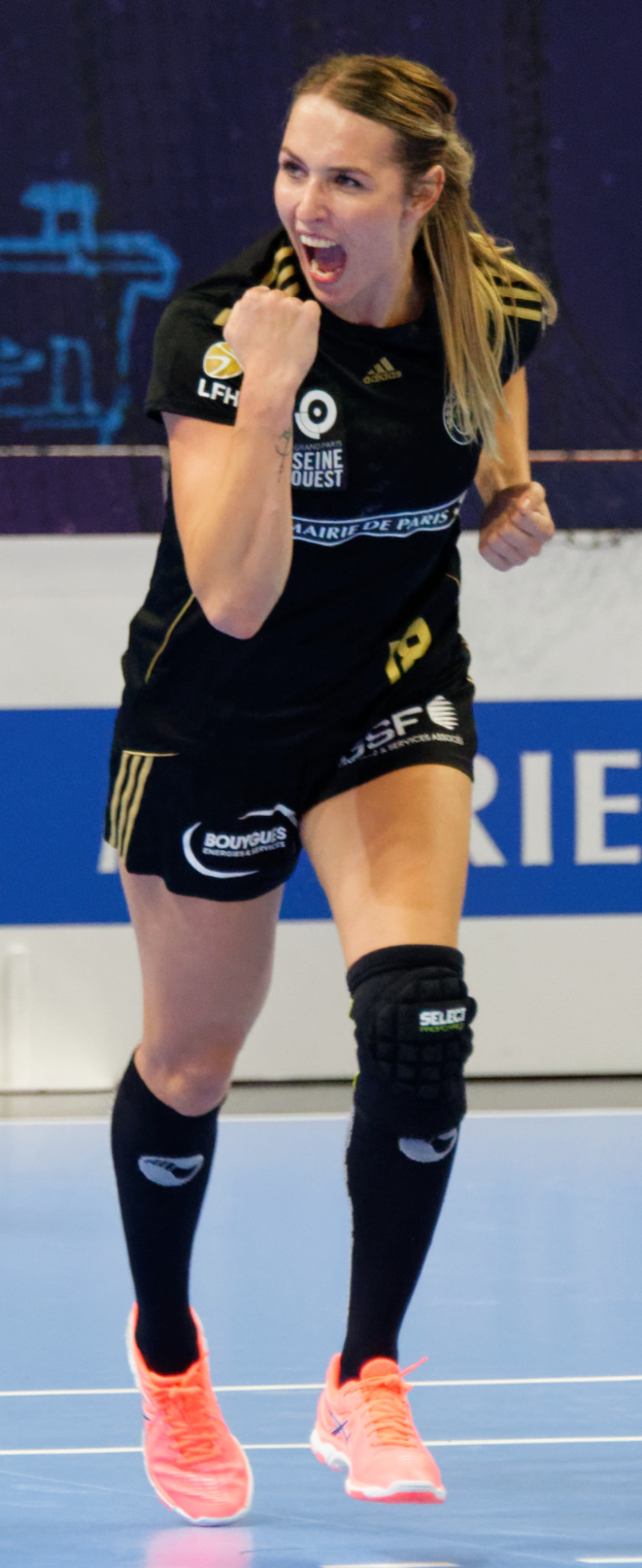Eine Frau in schwarzem Shirt und Shorts spielt Volleyball auf einem Court, mit einem Banner im Hintergrund.