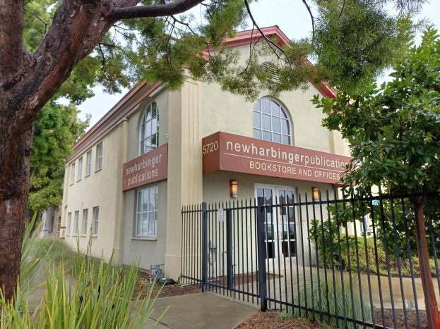 Außenansicht der Newharbinger Public Library in San Francisco, Kalifornien, mit einem Gebäude mit Fenstern und Türen, einer Schautafel, einem Metallzaun, einem Weg, Pflanzen, Bäumen und einem bewölkten Himmel.