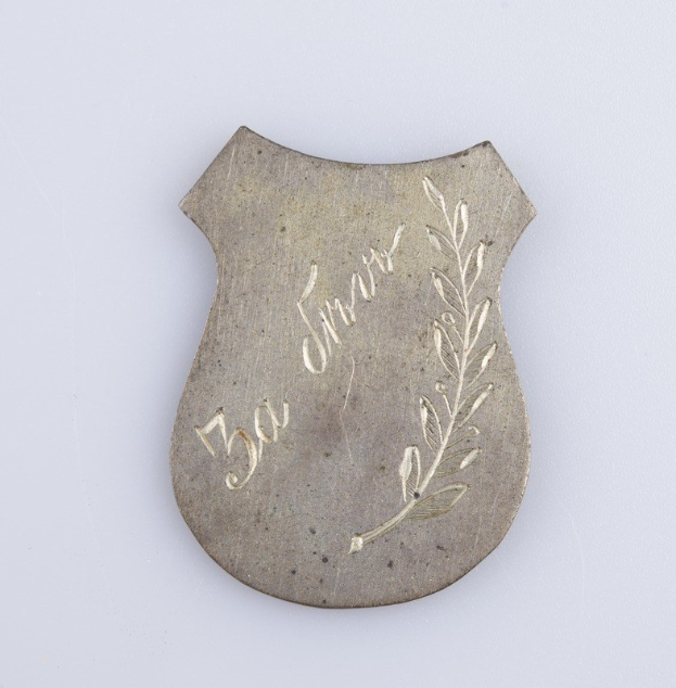 Ein silbernes Abzeichen mit einem Lorbeerkranz und der Inschrift "50. Hochzeitstag" auf einem weißen Hintergrund.