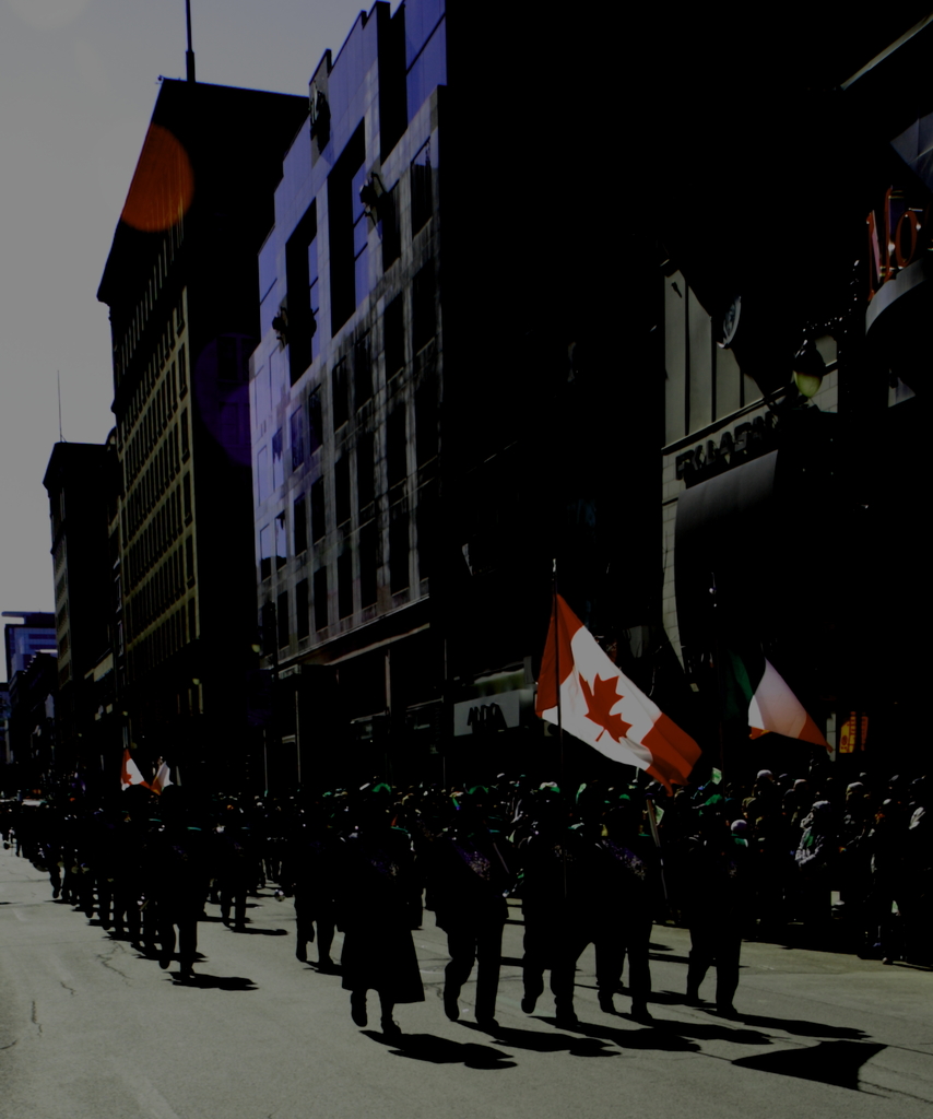 Eine Gruppe von Menschen marschiert auf einer Straße mit Fahnen, Gebäude mit Text darauf rechts und Himmel oben.