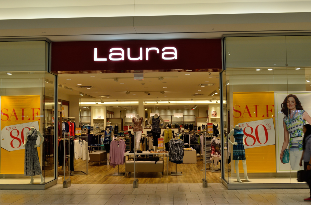 Ein Laura-Kleidungsgeschäft in einem Einkaufszentrum mit Schaufensterpuppen in Kleidern, hängenden Kleidern, Informationsschildern, Deckenleuchten und einer Person mit einer Tasche.