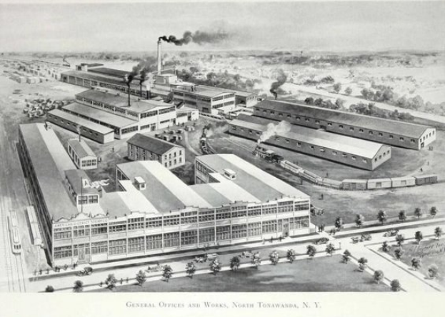 Luftaufnahme eines rauchenden Fabrikgebäudes umgeben von weiteren Gebäuden, Bäumen und Fahrzeugen auf der Straße mit der Beschriftung "General Office and Works, North Tonawanda, New York" unten.