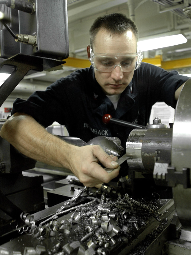 Ein Monteur mit Schutzbrille bedient eine Maschine in einer gut beleuchteten Fabrikumgebung.