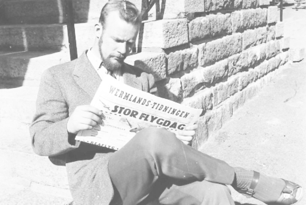 Schwarz-weiß-Foto eines Mannes in Anzug, der auf einer Treppe sitzt und eine Zeitung liest.