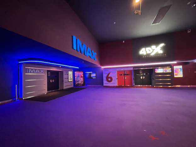 Innere eines Kinos mit lila Teppich, Text und Bildschirme an den Wänden und Deckenbeleuchtung.