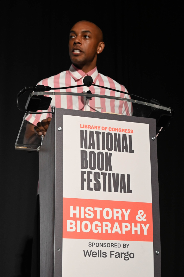 Ein Mann steht an einem Rednerpult mit einem Mikrofon und spricht bei einem Abendevent mit dem Titel "National Book Festival History & Biography".