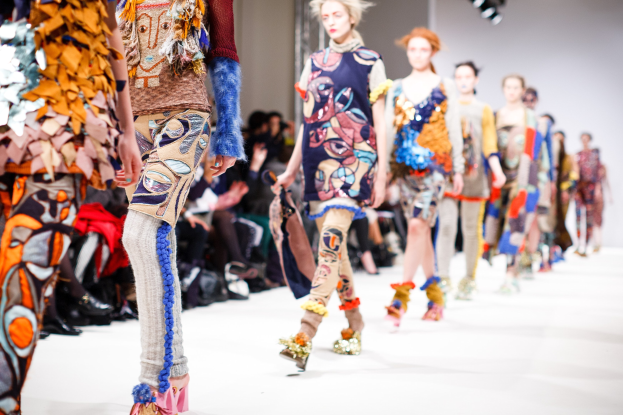 Eine Gruppe Von Frauen Geht Den Laufsteg Bei Der London Fashion Week Herunter, Mit Sitzenden Zuschauern Und Heller Beleuchtung Im Hintergrund, Erzeugt Ein Etwas Unscharfer, Traumhafter Effekt.