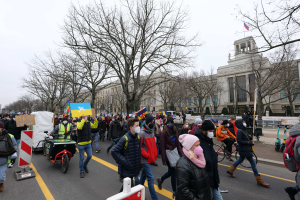 Eine große Gruppe von Menschen marschiert auf der Straße in Washington, D.C. am 21. Januar 2020 mit Schildern und Bannern, während einige Fahrräder fahren, Schilder, Bäume und ein klarer blauer Himmel im Hintergrund zu sehen sind.