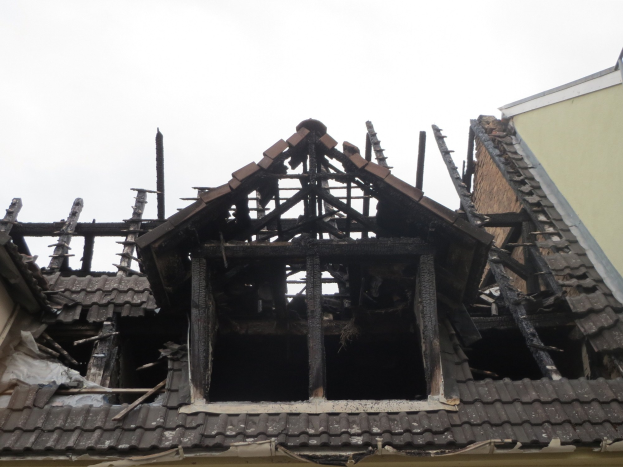 Ein Gebäude mit einem feuerbeschädigten Dach wird abgerissen, mit sichtbaren Trümmern und verstreuten Holzplanken gegen den Himmel.
