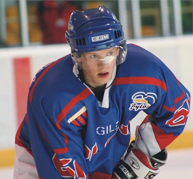 Ein Hockey-Spieler im Einsatz auf dem Eis, der einen Helm und Handschuhe trägt, mit unscharfem Hintergrund und Text oben und unten im Bild.