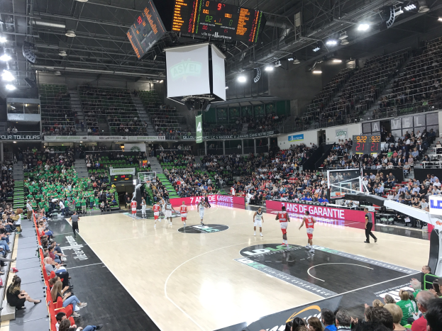 Basketballspiel in einer großen Arena mit Zuschauern, mit den Mannschaften Asvel und Galatasaray auf den Werbetafeln.