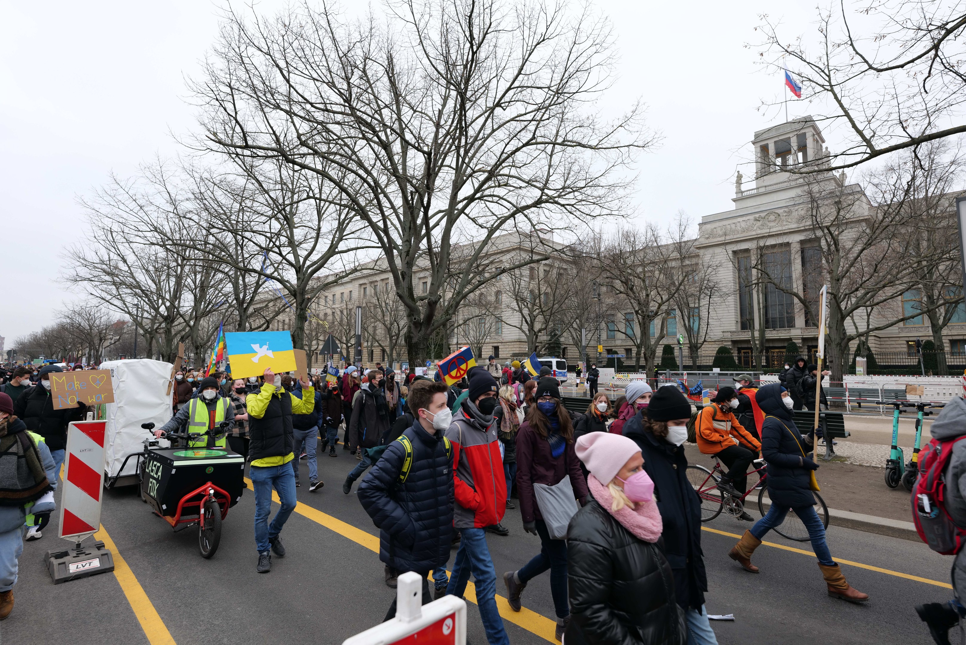 Eine große Gruppe von Menschen nimmt an einer Protestdemo in Washington, D.C. am 21. Januar 2020 teil und marschiert die Straße entlang, einige halten Schilder und Banner, andere fahren Fahrräder, mit Schildern, Bäumen und einem klaren blauen Himmel im Hintergrund.