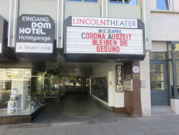 Außenansicht des Lincoln Theaters in Berlin, Deutschland, mit Glasfenstern und -türen sowie einer Schautafel und einem Innenblick auf eine belebte Stadtlandschaft.