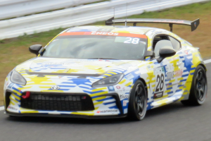 Ein weißer Toyota Supra GT3-Rennwagen mit Sponsorentext und Nummern auf einer Rennstrecke, umgeben von einer Begrenzung und Gras.