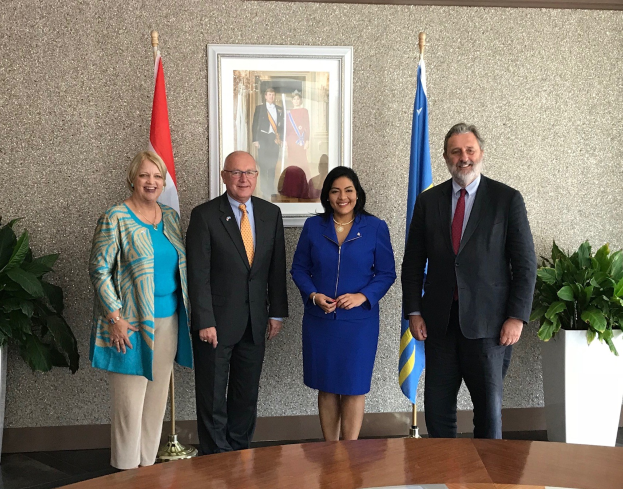 Eine Gruppe von Menschen, die lächeln und um einen Tisch mit Papieren stehen, umgeben von Fahnen, Topfpflanzen und einem Rahmenfoto an der Wand, was die Unterzeichnung eines U.S.-Kanada-Memorandums von Verständigung anzeigt.