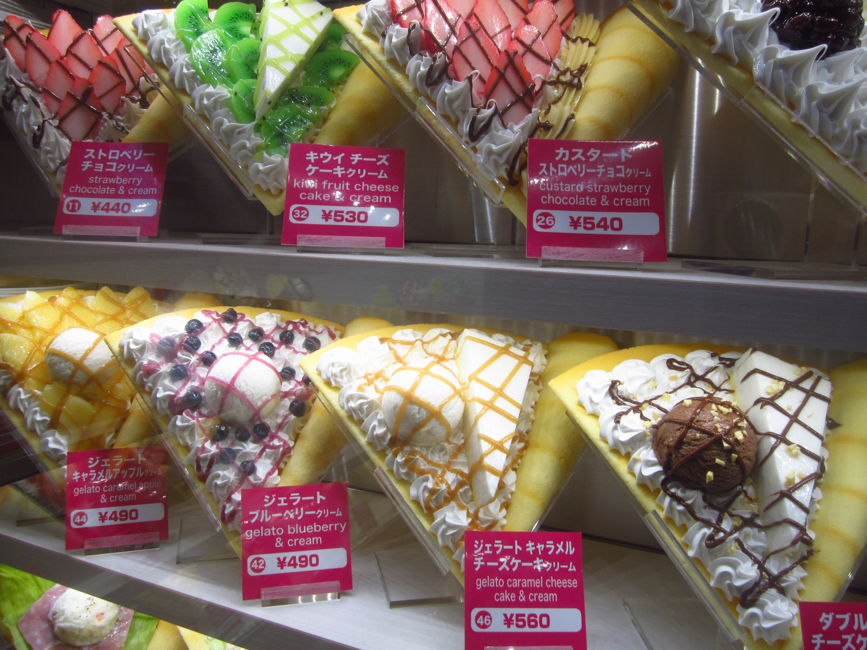 Vitrine voller verschiedener Eissorten, jede mit einem Preisschild, in unterschiedlichen Farben, Formen und Geschmacksrichtungen angeordnet.