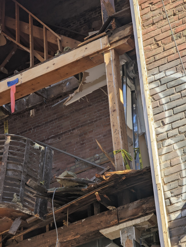 Teilweise abgerissenes Gebäude mit verstreuten Holzplanken und Schutt, zerbrochene Fenster und Türen.
