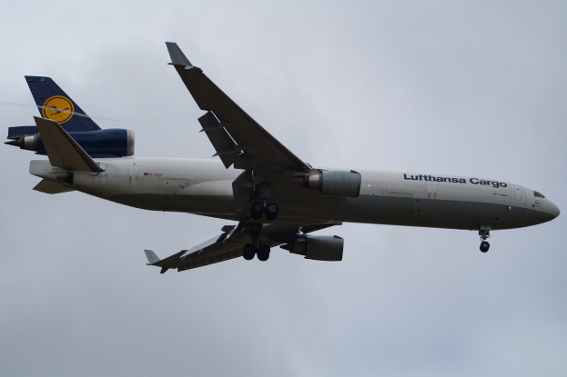 Ein Lufthansa Cargo Boeing 777-300ER im Flug, mit ausgefahrenen Flügeln und aktivierten Triebwerken, mit sichtbarem Text auf der Rumpfseite gegen einen wolkengefüllten Himmel.