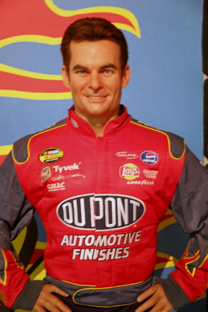 Ein Mann lächelt und trägt eine rote Jacke, mit einem blauen und roten Banner im Hintergrund.