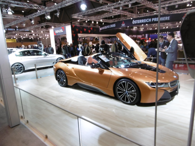 Ein elegantes, schwarzes BMW i8 Cabrio mit Chromakzenten auf der Internationalen Automobil-Ausstellung in Frankfurt, umgeben von formell gekleideten Gästen in einer Atmosphäre der Aufregung.