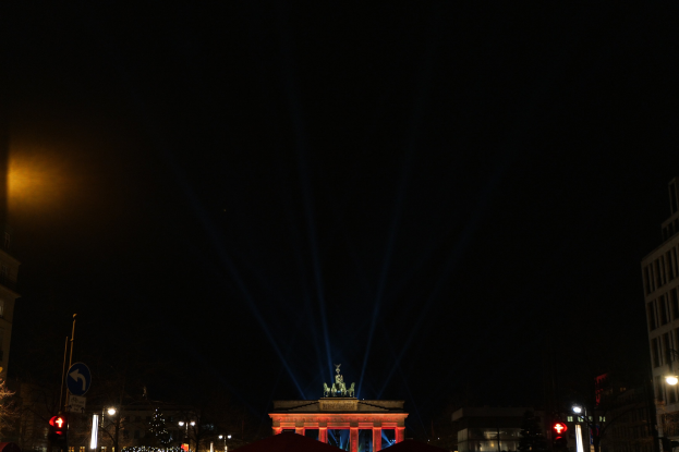 Das Brandenburger Tor in Berlin nachts, beleuchtet von Straßenlaternen und umgeben von Gebäuden, Bäumen, Pfählen, Verkehrsampeln, Schildern und Zelten unter einem dunklen Himmel.