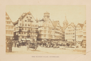 Altes Schwarz-Weiß-Foto eines belebten Marktplatzes in Stuttgart, Deutschland, mit mehrstöckigen Gebäuden, Passanten, horse-drawn carts und verschiedenen Marktständen; handgeschriebener Text erscheint entlang der unteren Kante.