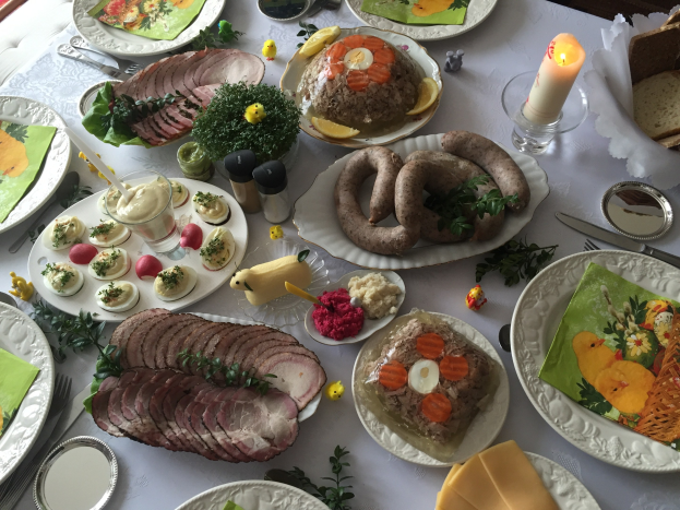Ein lang gedeckter Tisch mit verschiedenen Speisen, Besteck und Kerzen, umgeben von Stühlen, was auf ein traditionelles deutsches Osteressen hinweist.