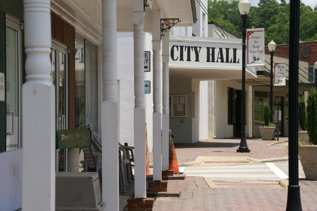 Stadthaus mit umgebender Infrastruktur, einschließlich Straßenlaternen, Schildern, Fahrzeugen, Verkehrskegeln, Stühlen, Topfpflanzen, Bäumen und einem bewölkten Himmel.