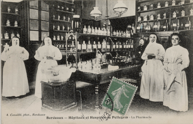 Ein Schwarz-Weiß-Foto einer Gruppe von Frauen, die um einen Tisch in einer Apotheke stehen, mit verschiedenen Gegenständen auf dem Tisch und Regalen mit Flaschen im Hintergrund, mit Text und einem Stempel unten auf dem Bild.