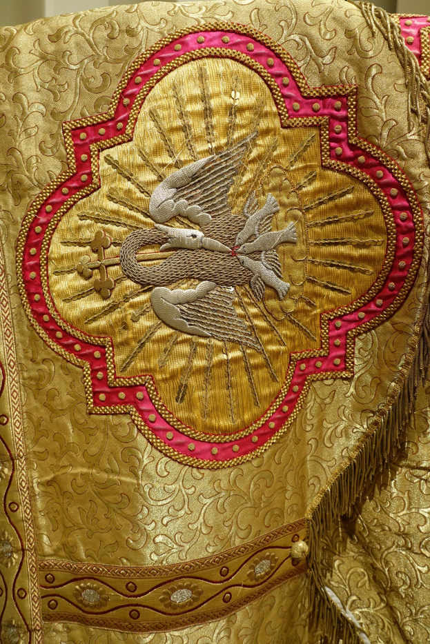 Nahaufnahme eines Priestergewandes mit goldenen und roten Stickereien und detaillierten Mustern, das an einer Wand hängt.
