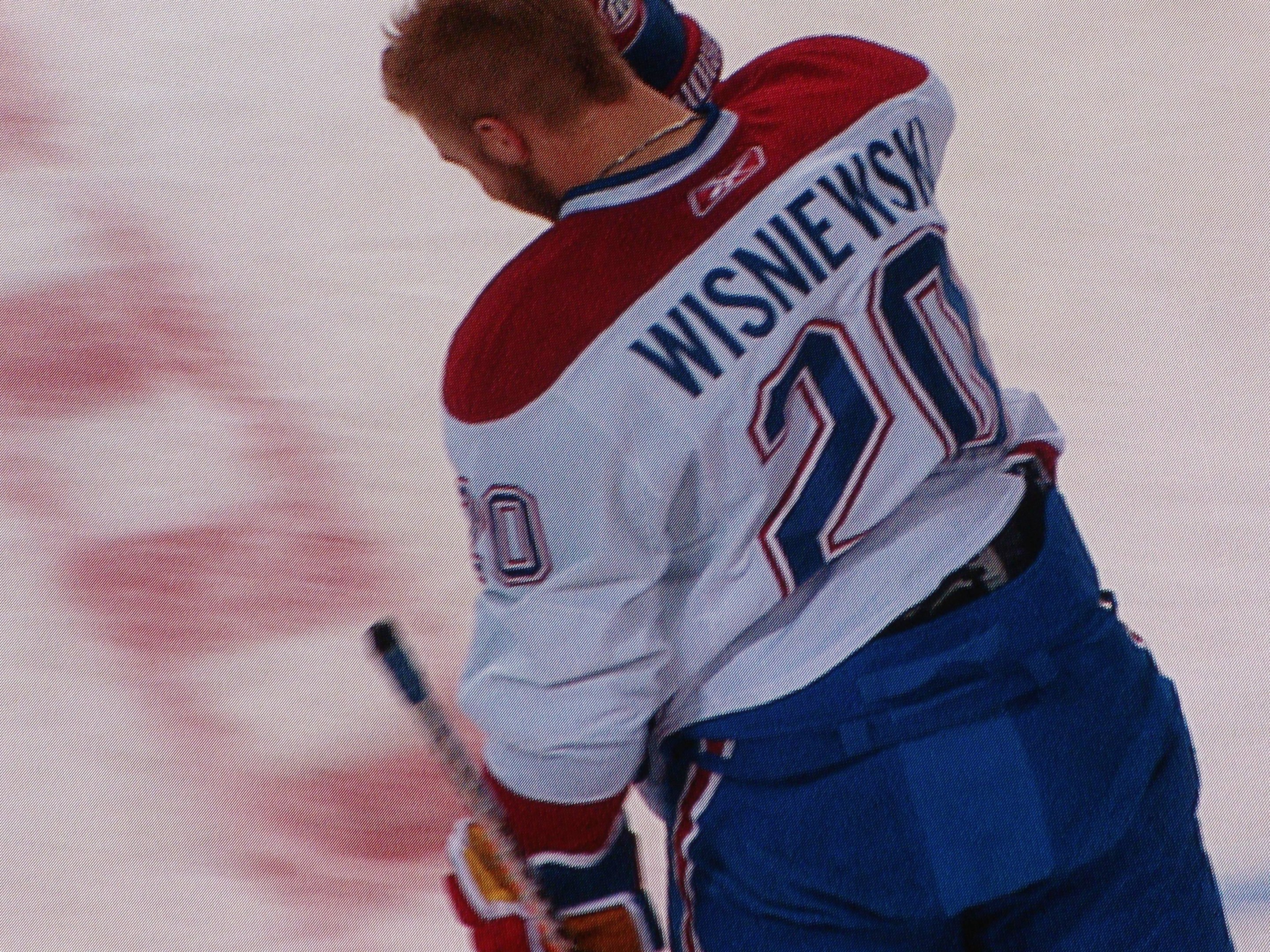 Ein Eishockeyspieler in einem "Wisniewski"-Trikot steht auf dem Eis, eine Hockey-Schläger haltend, mit konzentrierter und entschlossener Miene.