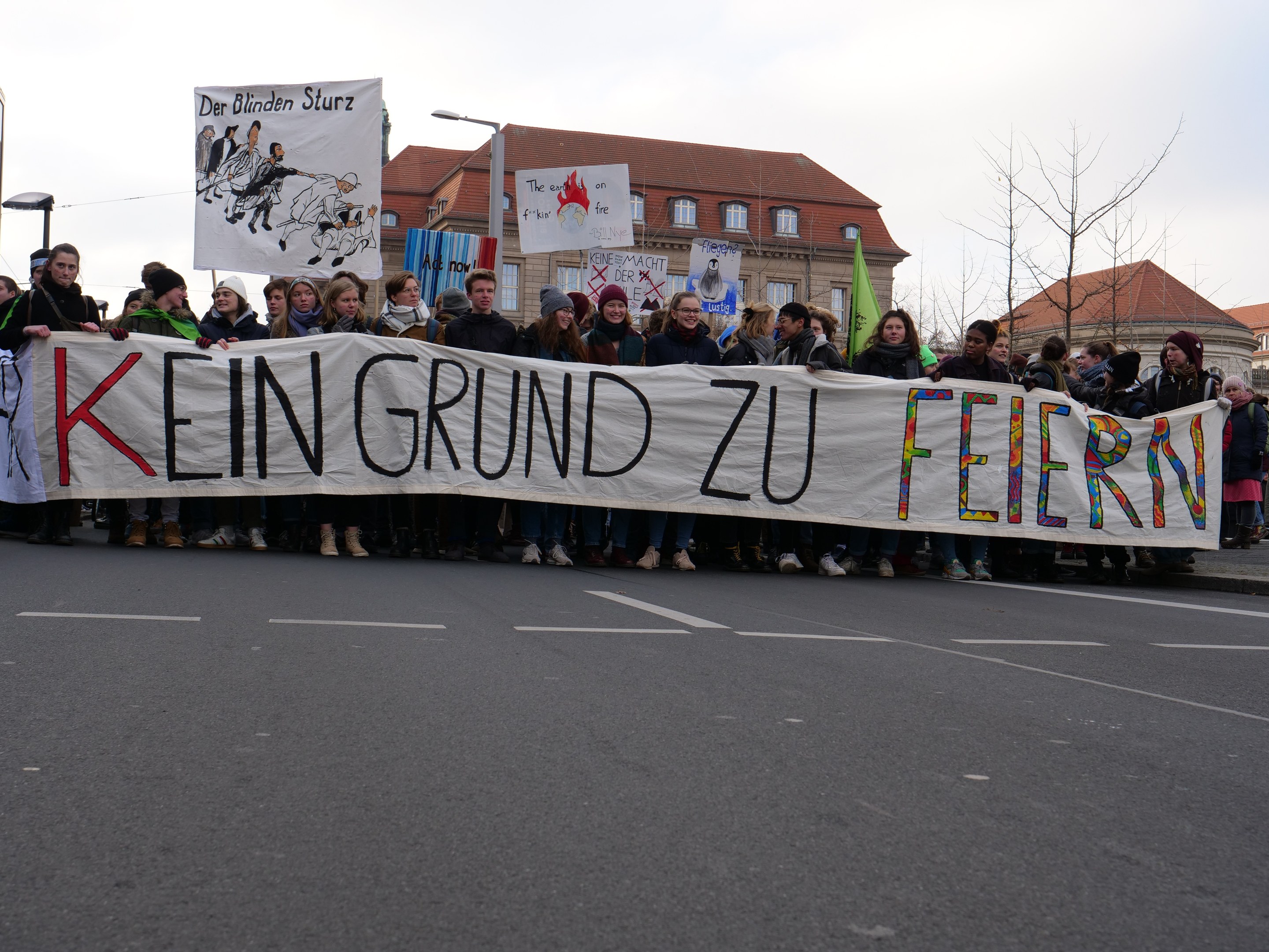 Demonstranten mit einem Transparent "Kein Grund zu Feiern" gegen deutsche Sparpolitik, mit Straßeninfrastruktur und Gebäuden im Hintergrund.