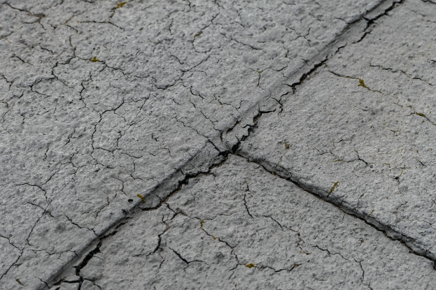 Nahaufnahme einer gebrochenen und unebenen Straßenoberfläche mit tiefen, breiten Rissen.
