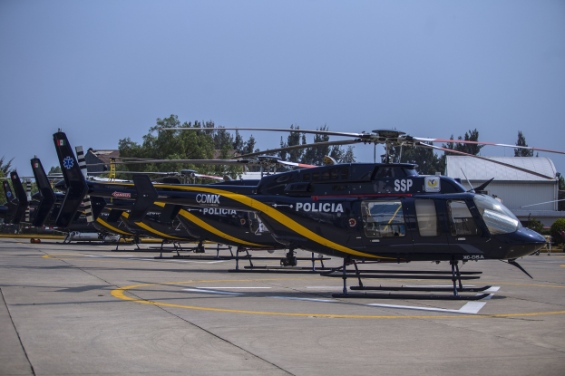 Mehrere Polizeihubschrauber auf einem Flughafenparkplatz geparkt, umgeben von Gebauden, Baumen und einem klaren blauen Himmel.