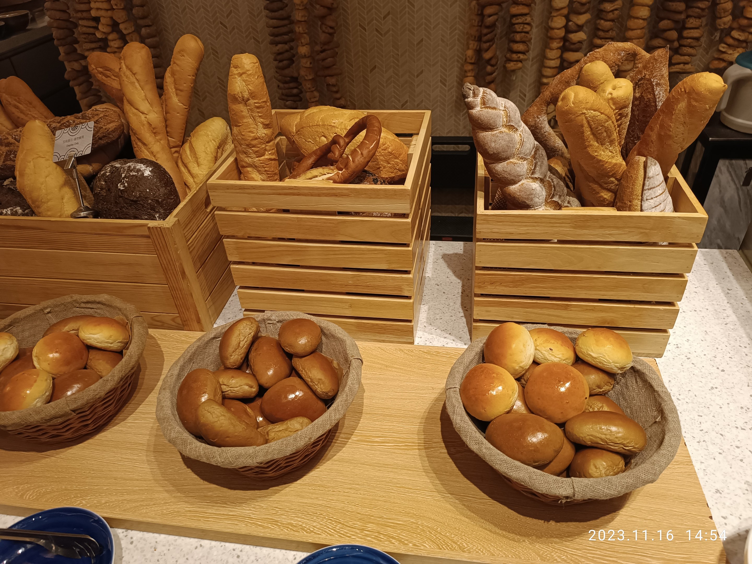 Holztisch mit Körben voller Brot, Tellern und Löffeln in einer Pariser Bäckerei mit einem wasserzeichenverzierten Hintergrund.