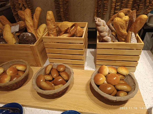 Holztisch mit Körben voller Brot, Tellern und Löffeln in einer Pariser Bäckerei mit einem wasserzeichenverzierten Hintergrund.