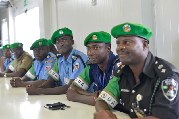 Gruppe von Polizeibeamten, die an einem Tisch während einer Schulung sitzen, mit Mobiltelefonen und anderen Gegenständen auf dem Tisch, in einem Raum mit Fenstern und Deckenleuchten.
