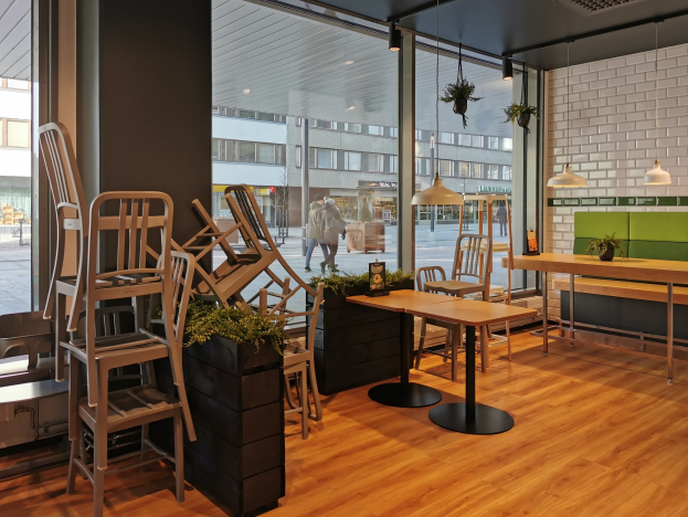 Ein Restaurantinnenraum mit hölzernen Tischen und Stühlen in der Nähe eines großen Fensters, das auf eine Straße mit Fußgängern, Gebäuden und städtischen Elementen in Berlin, Deutschland, hinausgeht.